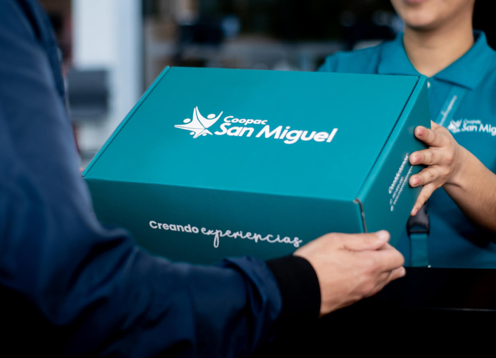 Persona recibiendo un paquete azul de Coopac San Miguel con el logo y mensaje creando experiencias