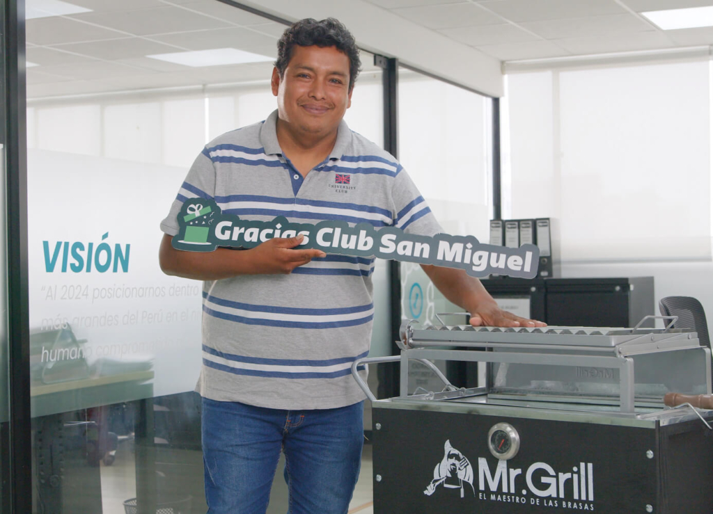 Persona ganadora sosteniendo cartel de agradecimiento al Club San Miguel junto a una parrilla de premio