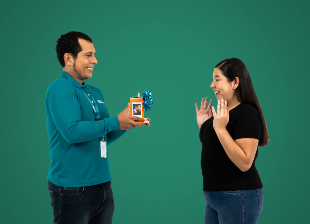 Colaborador de Coopac San Miguel entrega un regalo sorpresa a una socia, generando una expresión de alegría en un fondo verde institucional