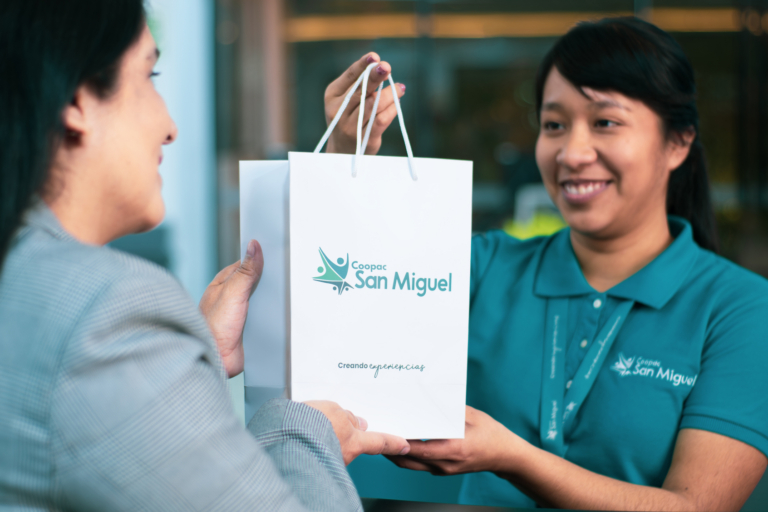 Asesora de Coopac San Miguel entregando una bolsa institucional a una socia, representando los beneficios y atención personalizada al invertir en un Depósito a Plazo Fijo