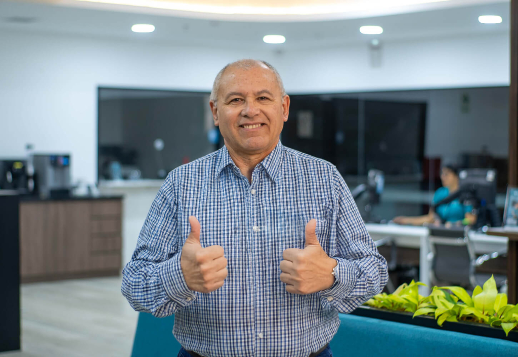 Socio adulto mayor sonriendo con pulgares arriba en una agencia de Coopac San Miguel, reflejando confianza y transparencia en la atención