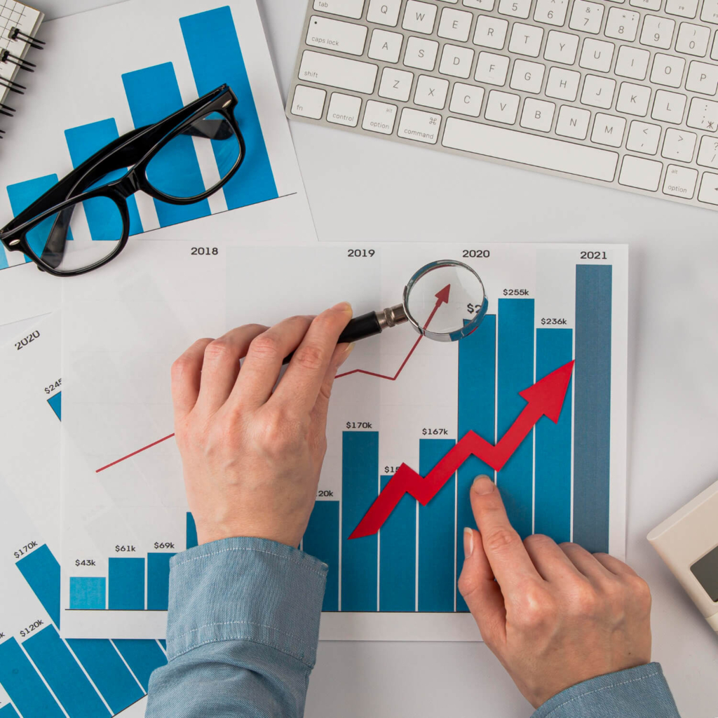 Manos analizando gráficos financieros de crecimiento con lupa y flechas, simbolizando los resultados de la Memoria Anual 2023 de Coopac San Miguel