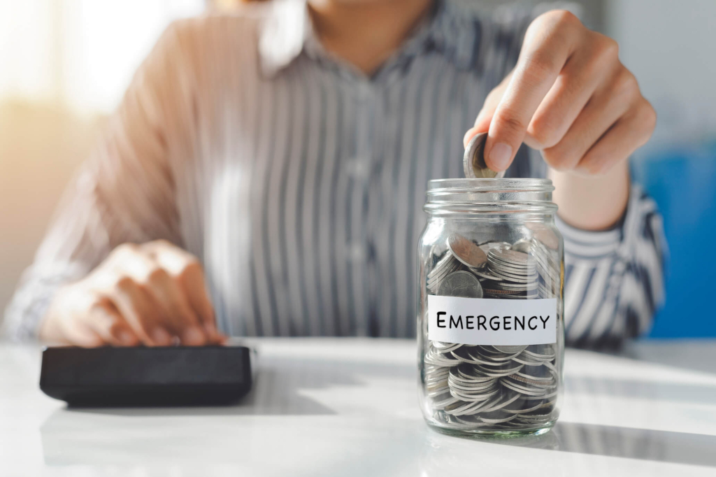 Persona depositando monedas en frasco etiquetado como fondo de emergencia, ideal para imprevistos con el respaldo de Coopac San Miguel