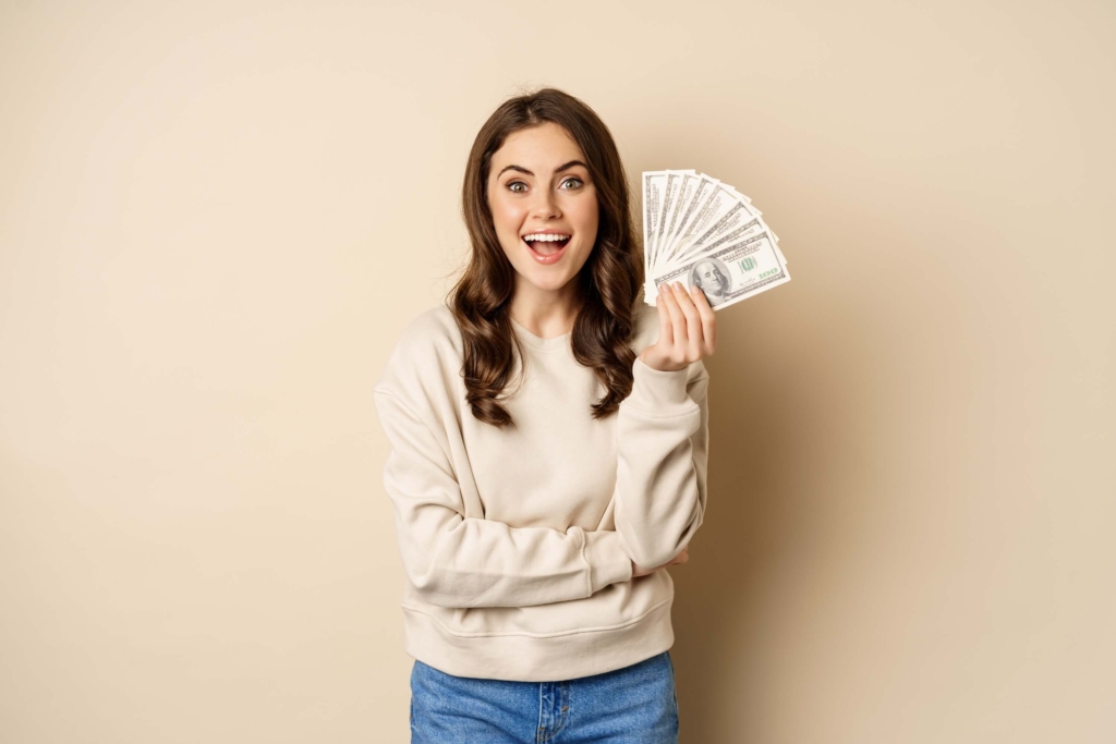 Mujer sonriente sostiene varios billetes en la mano, representando préstamos personales con tasas competitivas de la Cooperativa San Miguel