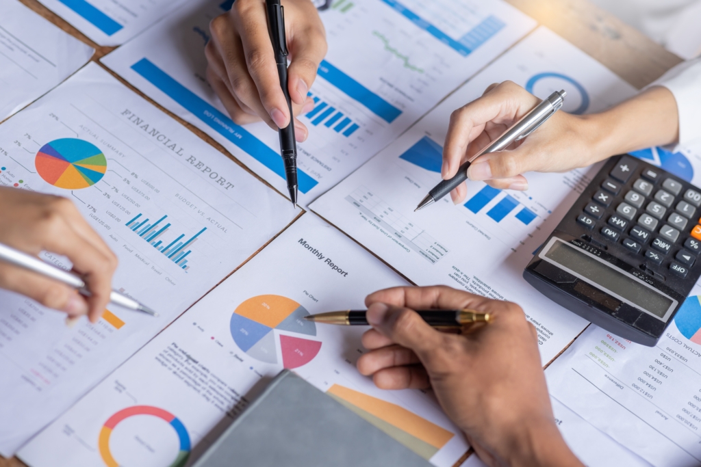Manos de varias personas revisando informes financieros con gráficos y tablas, junto a una calculadora, usada en una entrada sobre la Clasificación de Riesgo en el Sector Cooperativo