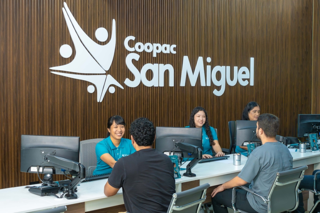 Personal de Coopac San Miguel en las oficinas de Av. Faustino Sánchez Carrión 419 Magdalena del Mar atendiendo sonrientes en ventanilla con el logo institucional visible en el fondo.